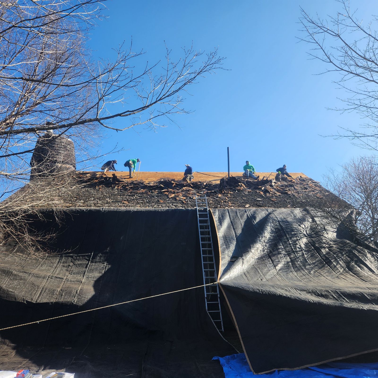 Crew stripping the cedar roof with the building wrapped in tarps