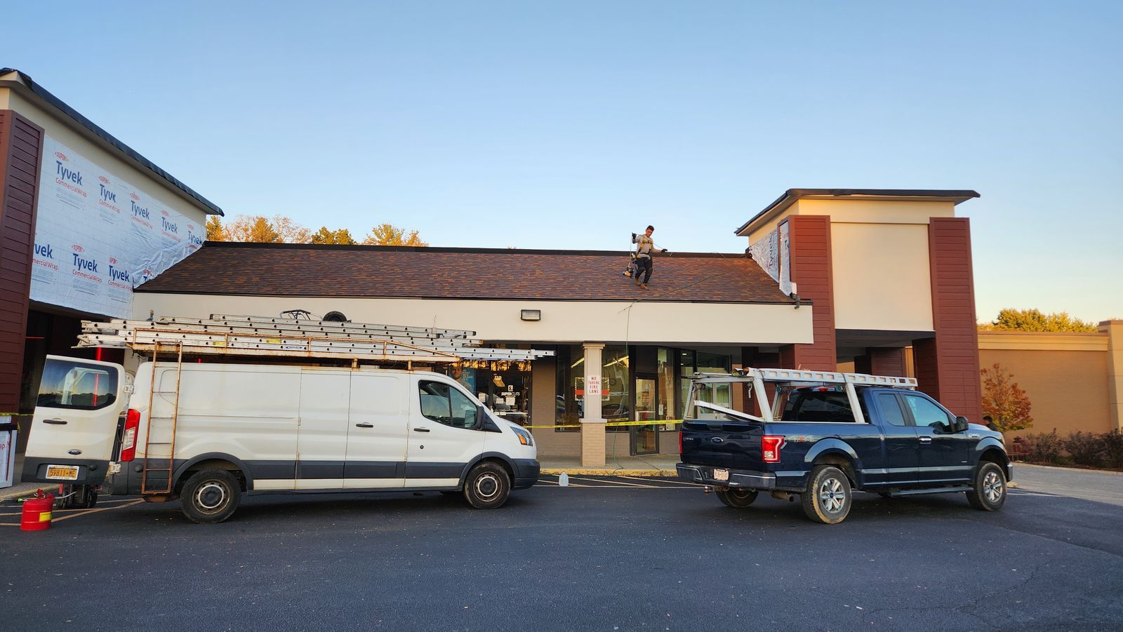Roofer tied off on a commercial retail building roof at dusk