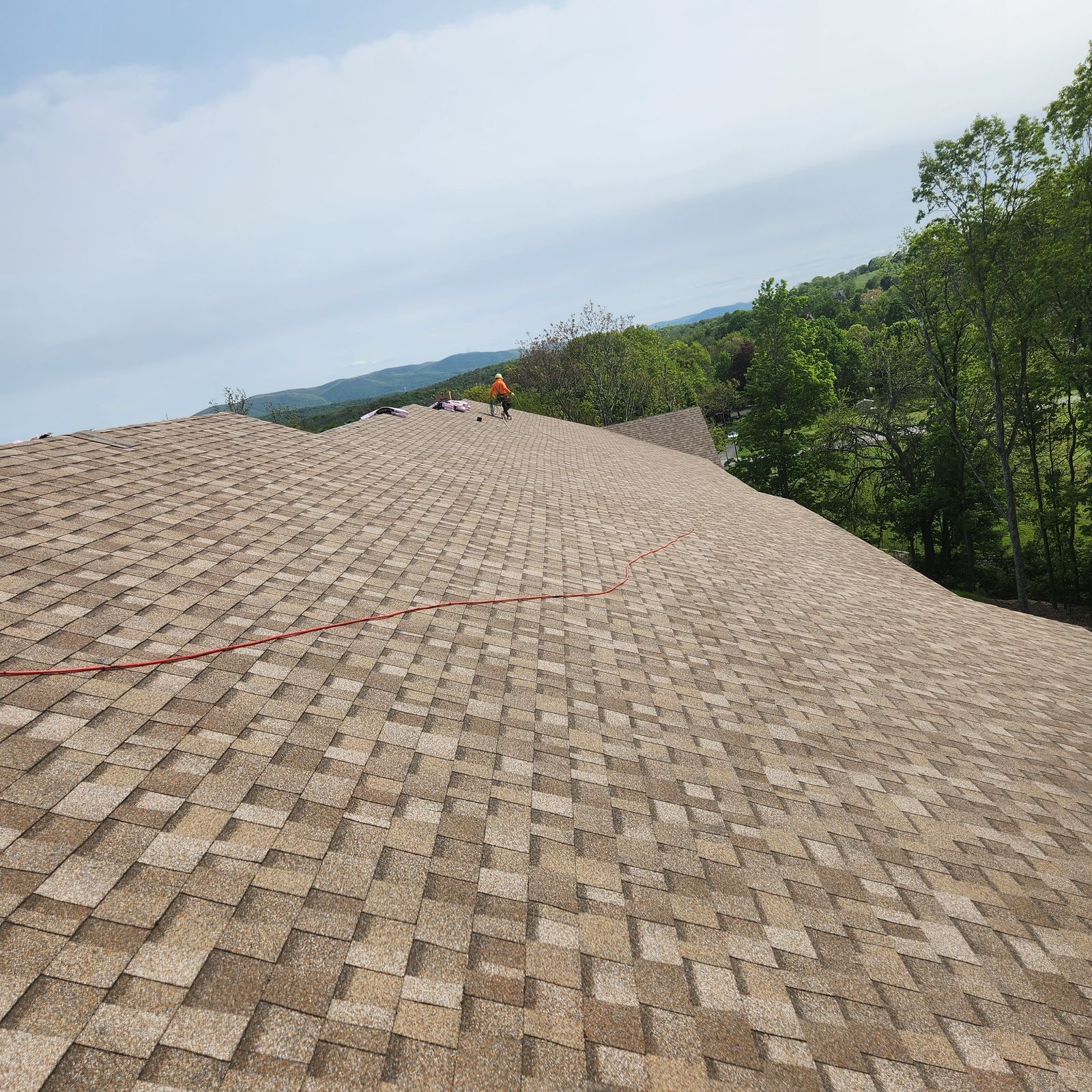 Roofer walking the ridge of a very large shingle roof with mountains behind