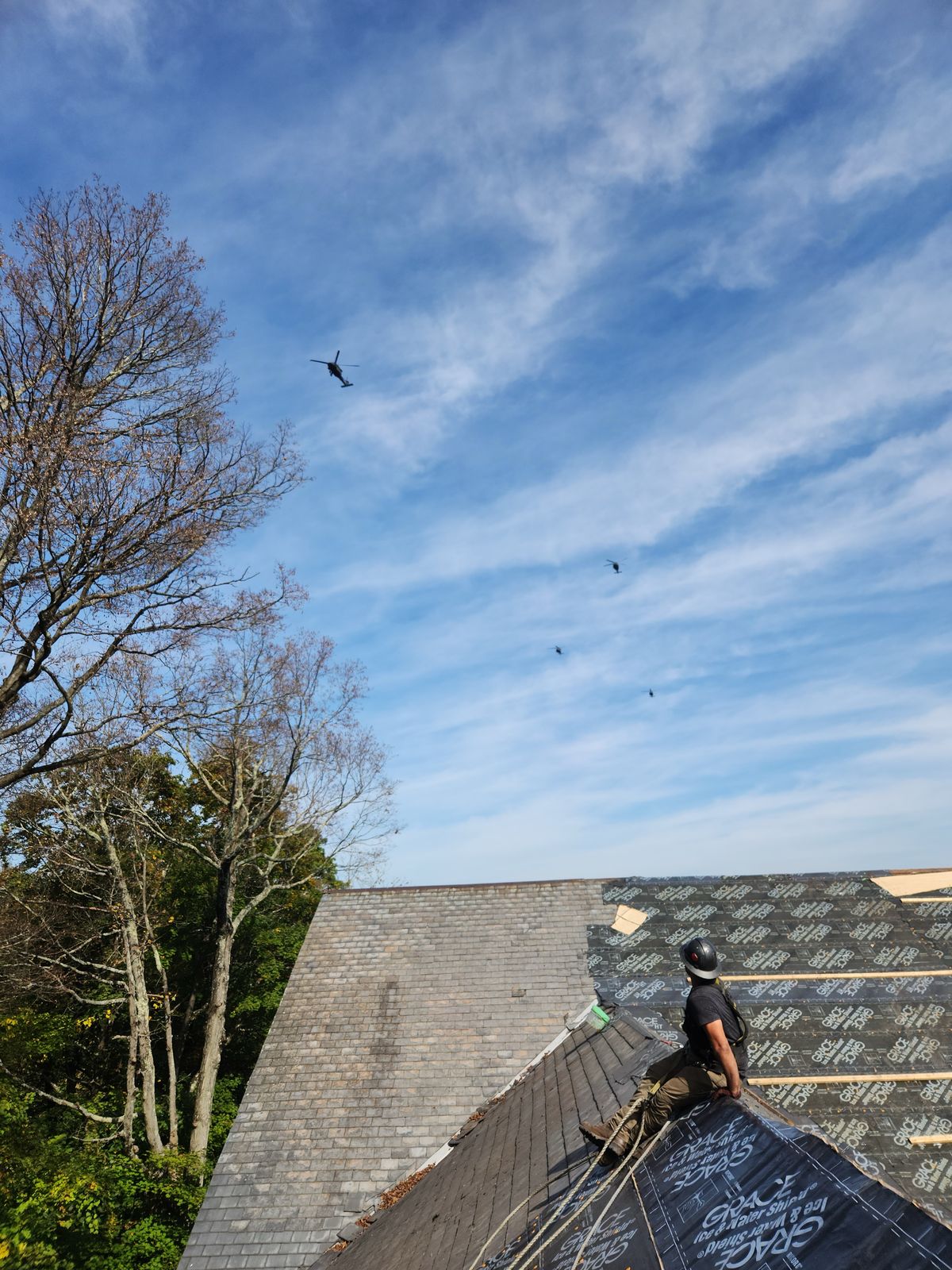 Roofer seated on a landmark slate roof watching a formation of Black Hawk helicopters fly past